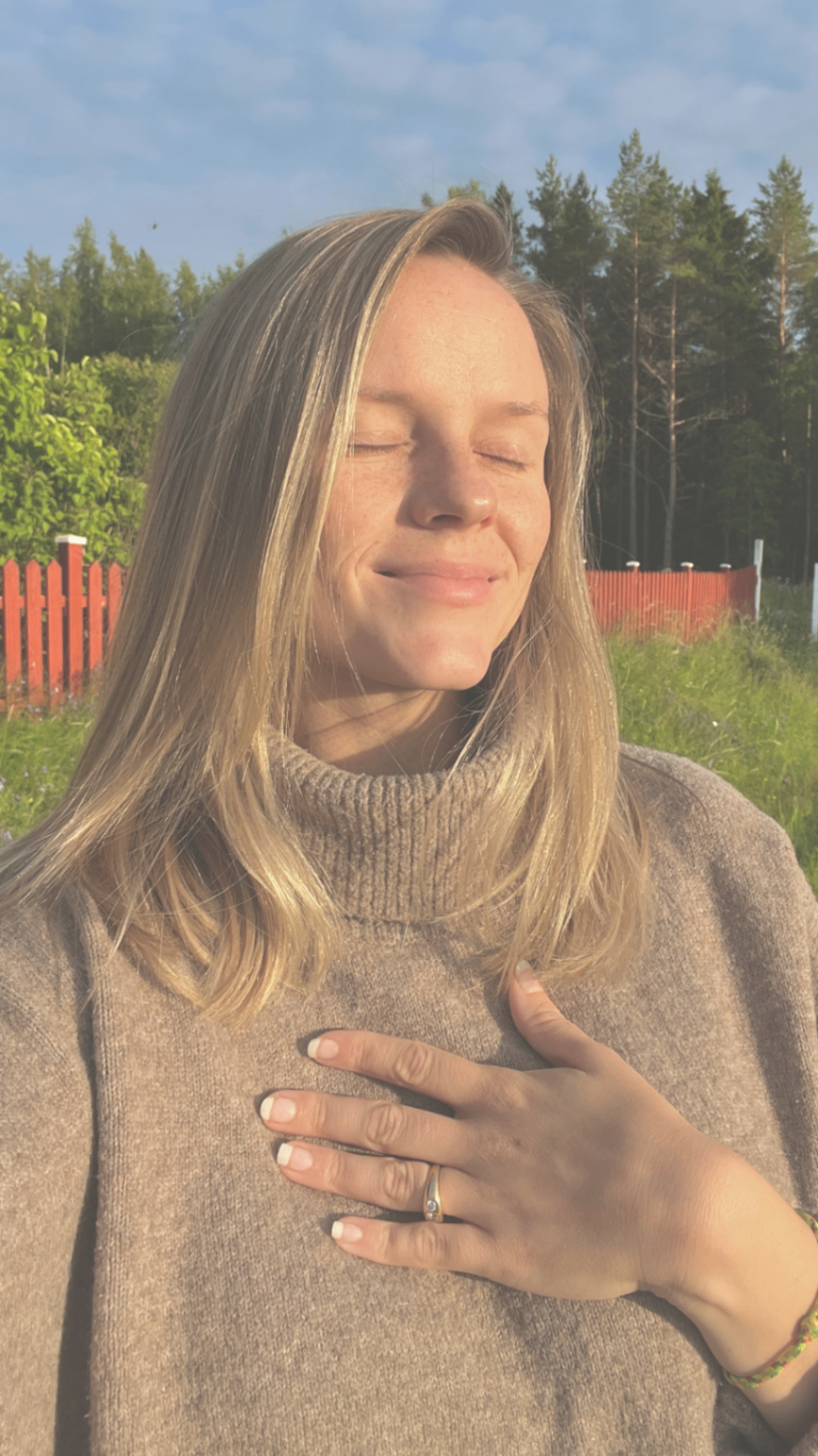 Alexandra står utomhus i kvällssol med slutna ögon och handen på hjärtat