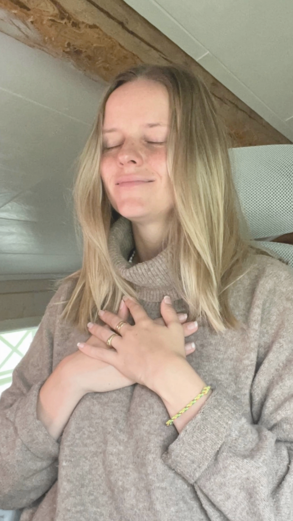 Alexandra sitter inomhus med slutna ögon och båda händerna på hjärtat